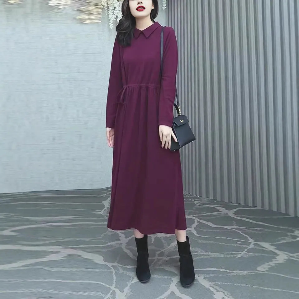 A woman wearing a solid purplish-red long-sleeve maxi dress, showcasing its extra-long sleeves and full-length skirt.