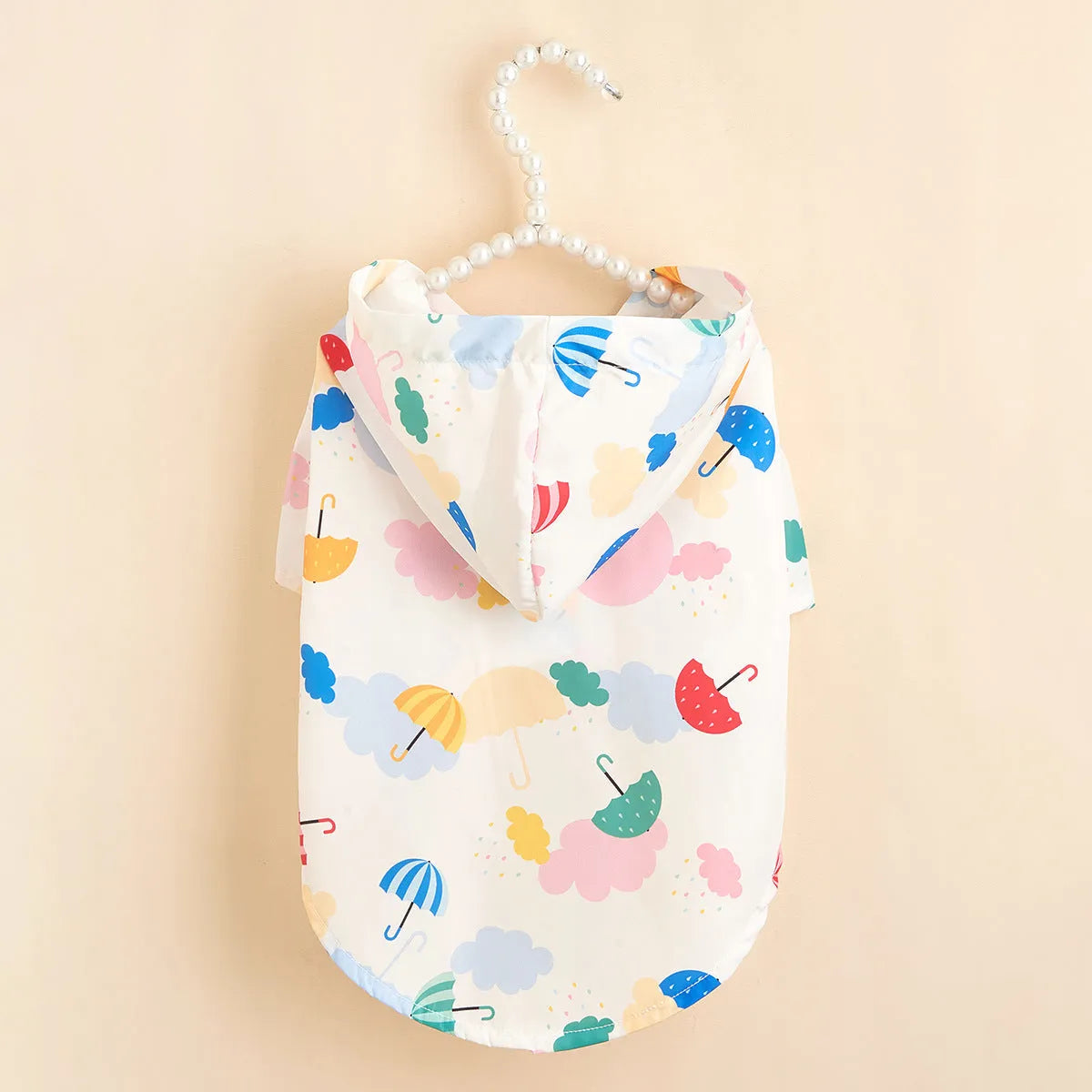 Small white dog wearing a colourful cartoon umbrella pattern polyester raincoat outdoors.