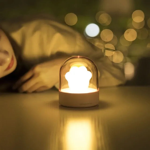 Pink cat paw shaped USB rechargeable night light with soft glow on a desk.