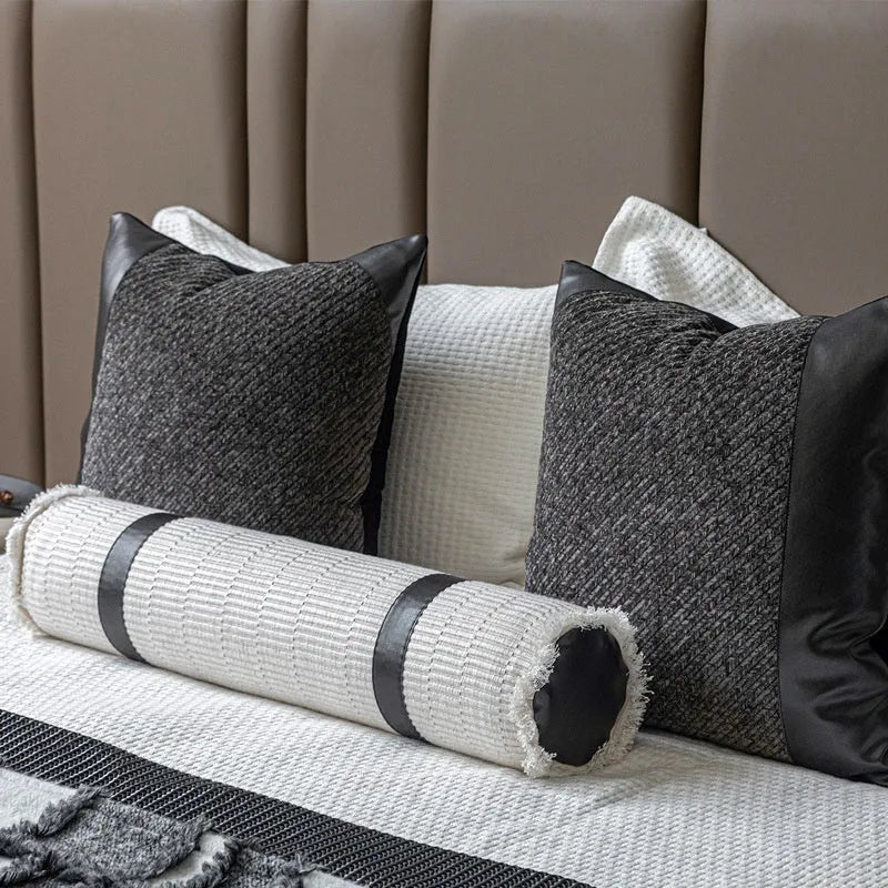 Grey and white plaid bed runner blanket with matching pillowcase and brown leather round pillow on a bed.