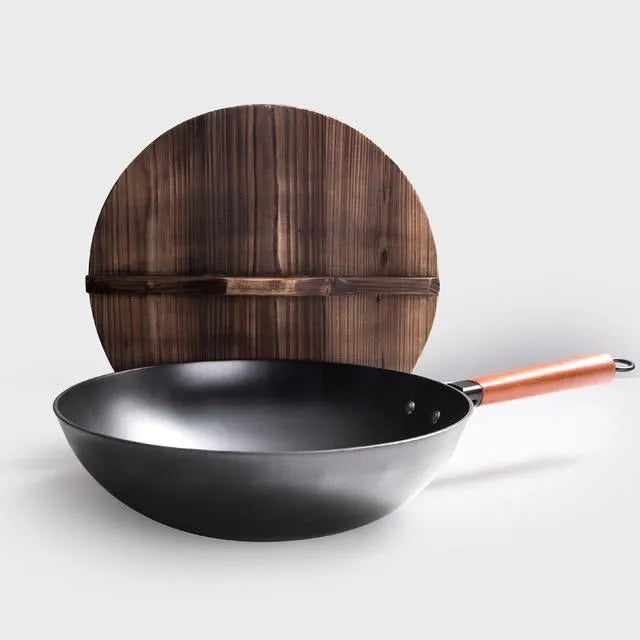 Handmade black iron wok pan with a long wooden handle on a kitchen counter.