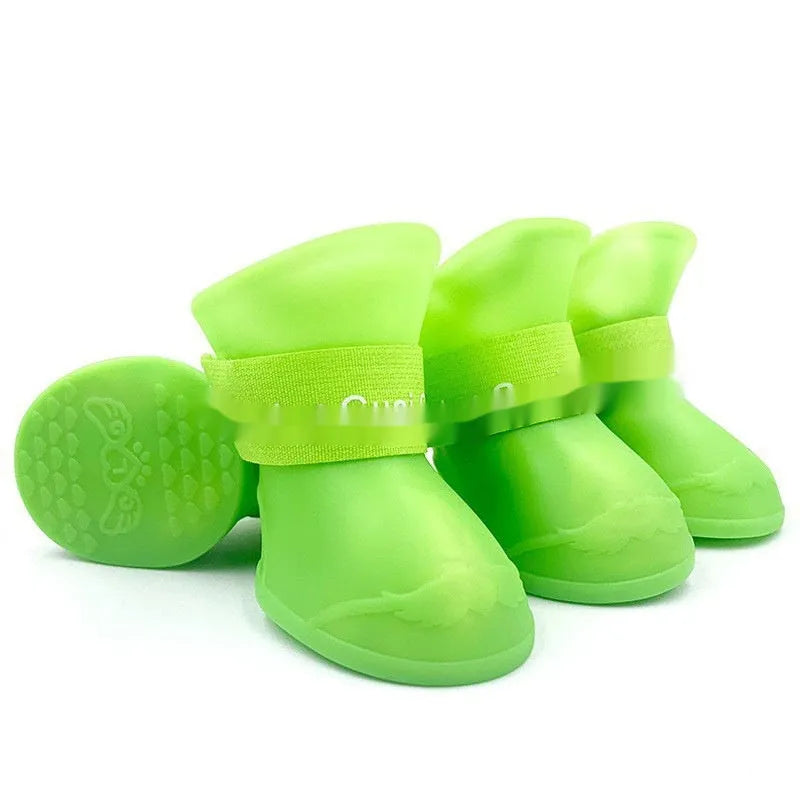 Set of four colourful rubber dog rain shoes with anti-slip soles on a wet surface.
