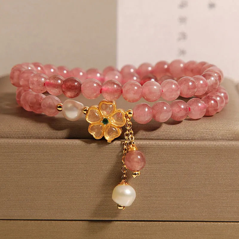 Women's double ring bracelet with strawberry quartz four-leaf clover charms on wrist.
