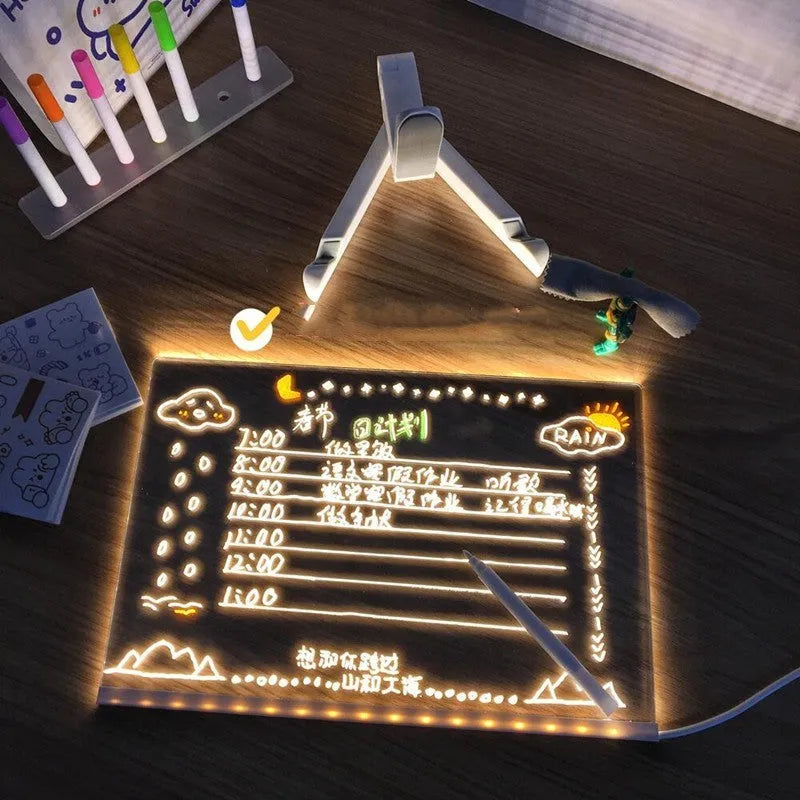 Acrylic DIY LED message board on a bracket, glowing softly with handwritten notes, alongside white and colourful pens.