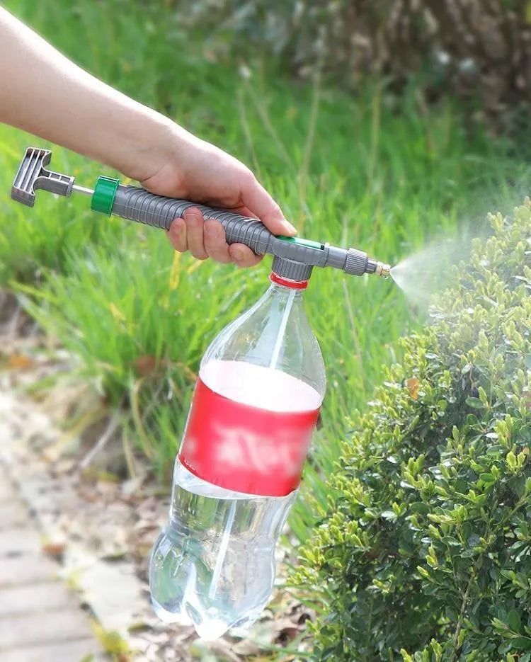 Plastic watering sprayer nozzle with extension tube attached to a large clear beverage bottle.