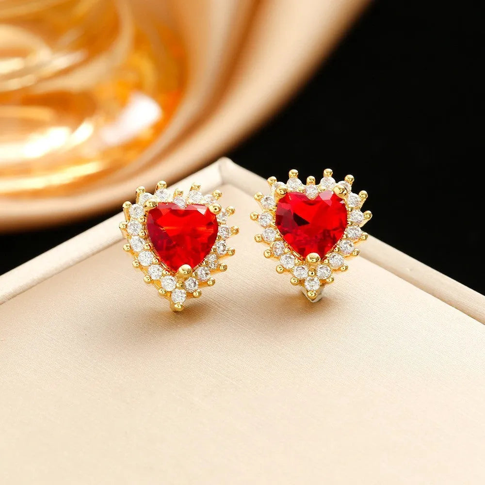 Gold red titanium steel necklace with heart and flower pendant, matching stud earrings, and ring on a grey background.