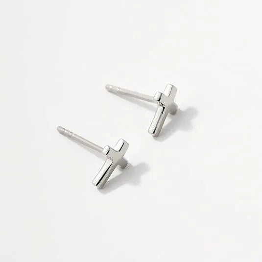 Women's gold bow stud earrings and silver cross stud earrings on a flat surface.