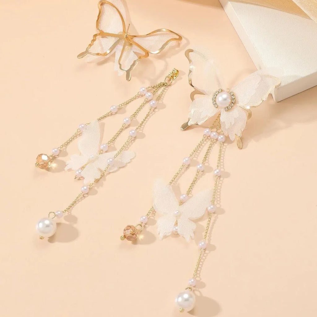 White butterfly-shaped dangling earrings with rhinestones, a pearl, and a fine chain on a plain background.