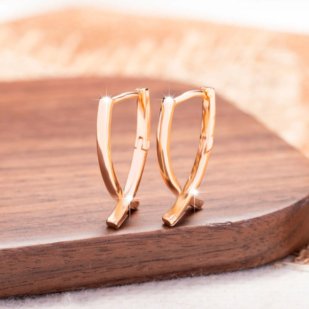 Close-up of a pair of rose gold cross drop earrings on a white background, showing post fittings.