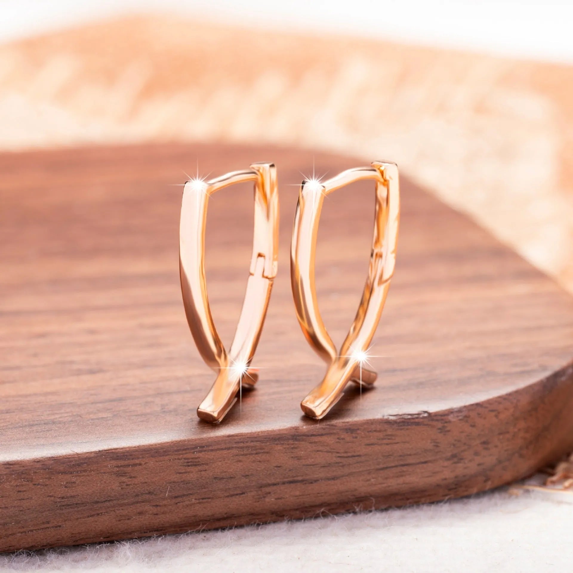 Close-up of a pair of rose gold cross drop earrings on a white background, showing post fittings.