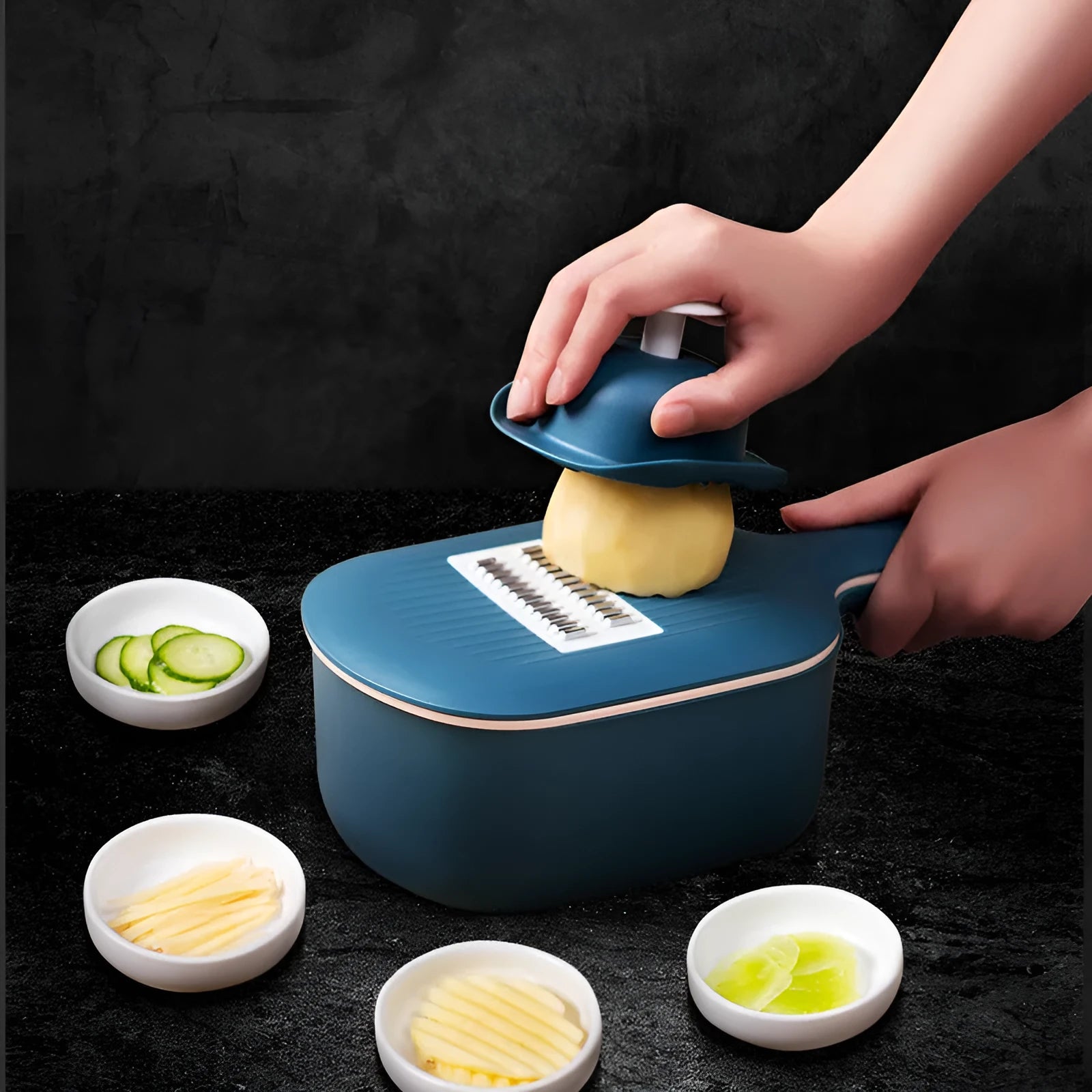 Dark blue vegetable cutter with four stainless steel blades, a hand guard, and a drain basket on a kitchen counter.