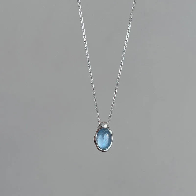 Close-up of a navy blue and platinum coloured water drop pendant necklace with an adjustable cross chain on a person's collarbone.