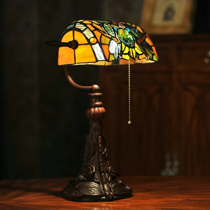 Tiffany style table lamp with colourful stained glass shade and resin base on a wooden desk