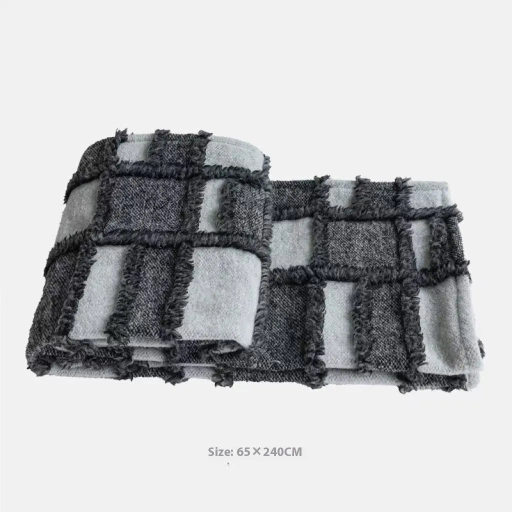 Grey and white plaid bed runner blanket with matching pillowcase and brown leather round pillow on a bed.