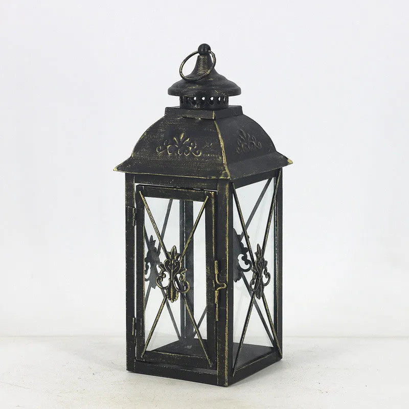 Black wrought iron floor-standing storm lantern with clear tempered glass panels on a garden patio.