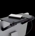 Black adjustable screen top shelf on a desktop monitor holding a streaming device and remote