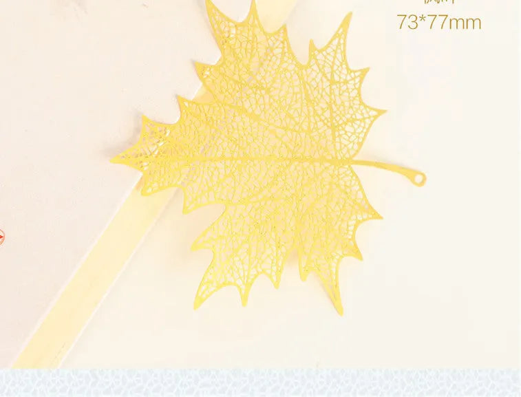 Detailed brass bookmark with hollow maple leaf pendant and rose gold tassel on a book page.