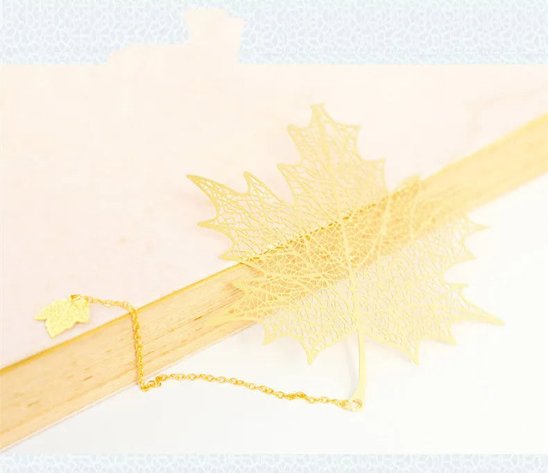 Detailed brass bookmark with hollow maple leaf pendant and rose gold tassel on a book page.