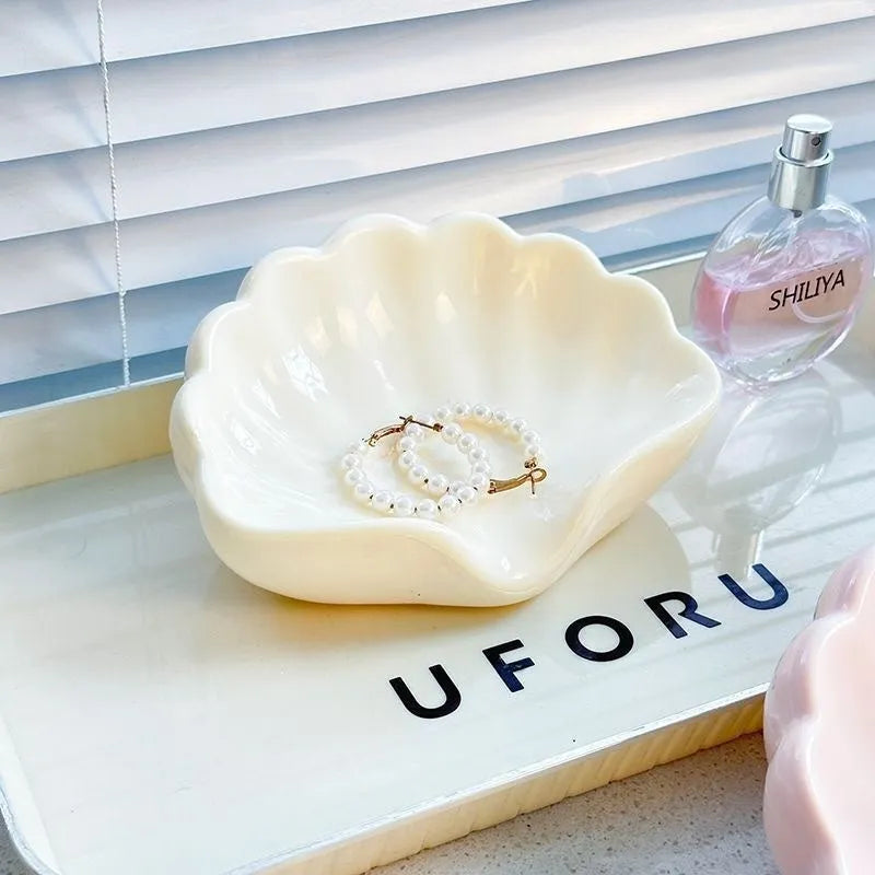 White or pink plastic shell-shaped soap dish for bathroom use on a counter.