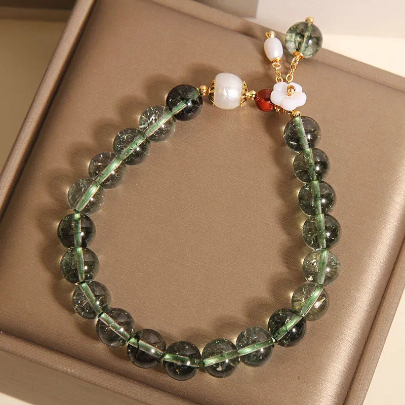 Women's green phantom quartz crystal bracelet with small shell flower accent on wrist.
