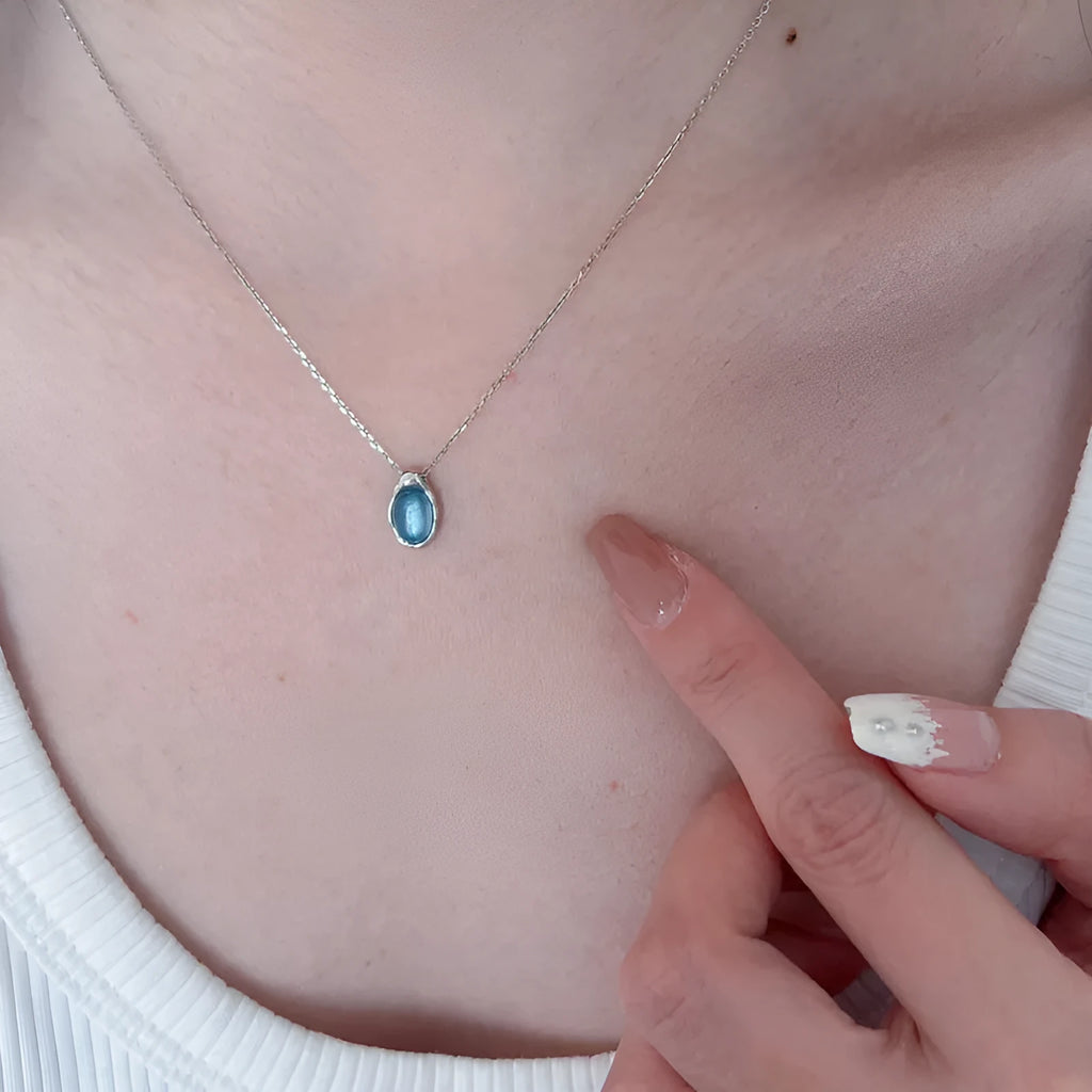 Close-up of a navy blue and platinum coloured water drop pendant necklace with an adjustable cross chain on a person's collarbone.