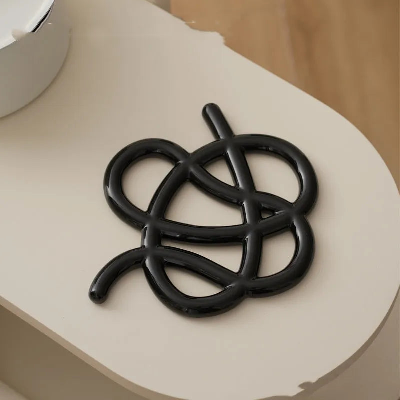 Irregular-shaped ceramic heat proof mat in grey with a curved hook for hanging, sitting on a wooden table.