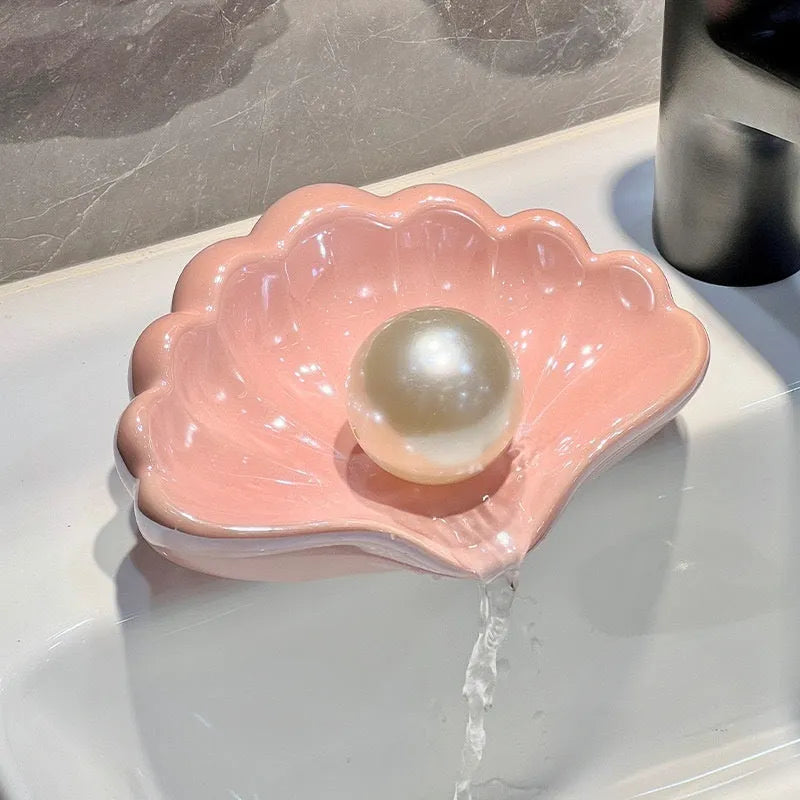 White or pink plastic shell-shaped soap dish for bathroom use on a counter.