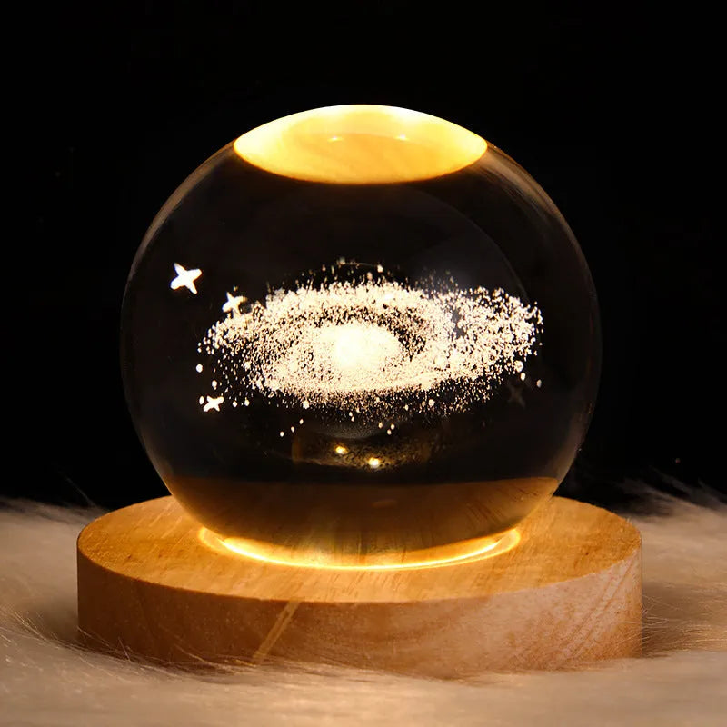 Clear crystal ball LED night light showing a 3D galaxy or planet design, lit from within on a table.