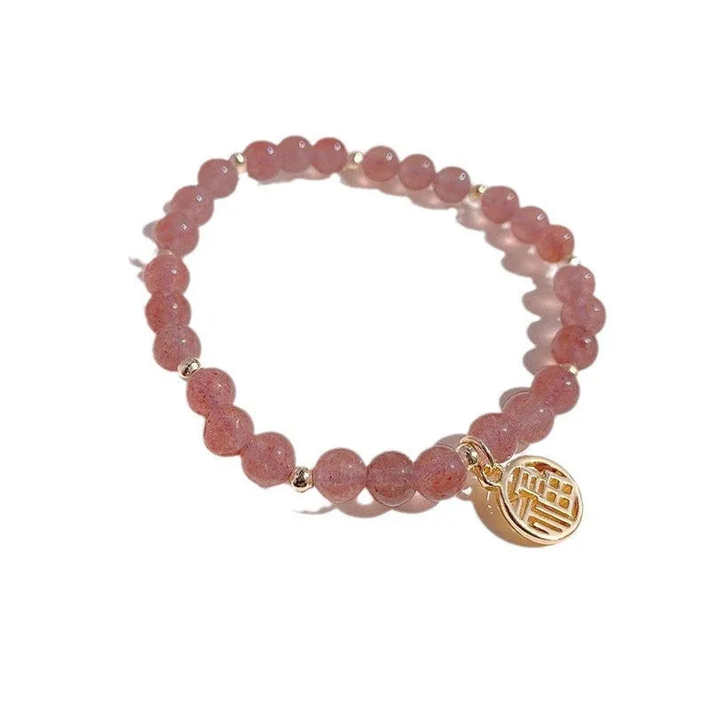 Glass strawberry quartz bead bracelet with a blessing card charm on a wrist.
