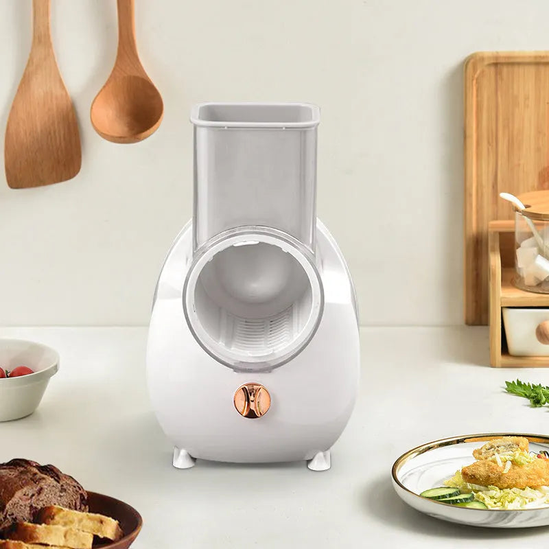 White electric rotary vegetable slicer with suction base and interchangeable blades on a kitchen counter.