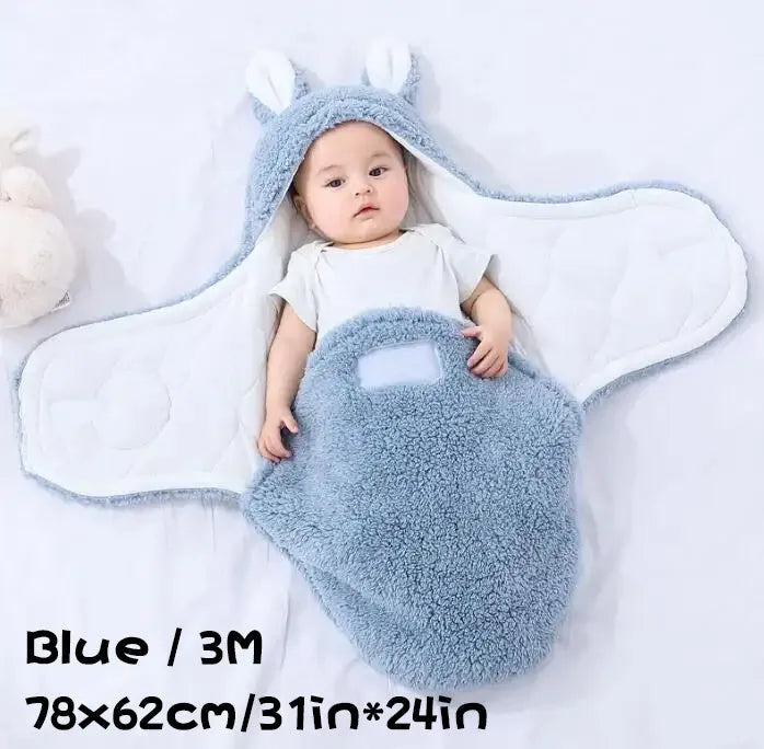 Baby wearing a blue adjustable cotton sleep sack with velcro swaddle closures and a head-protecting hood.