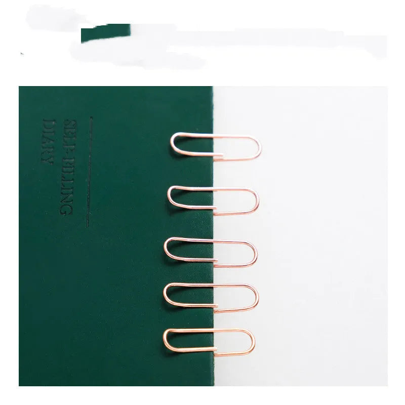 100 rose gold coloured heart-shaped metal paper clips in a box.