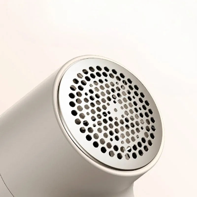 White electric lint remover with LED display showing battery level, placed beside clothing with fabric pilling