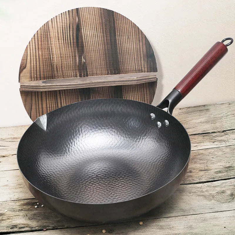 Handmade black iron wok pan with a long wooden handle on a kitchen counter.