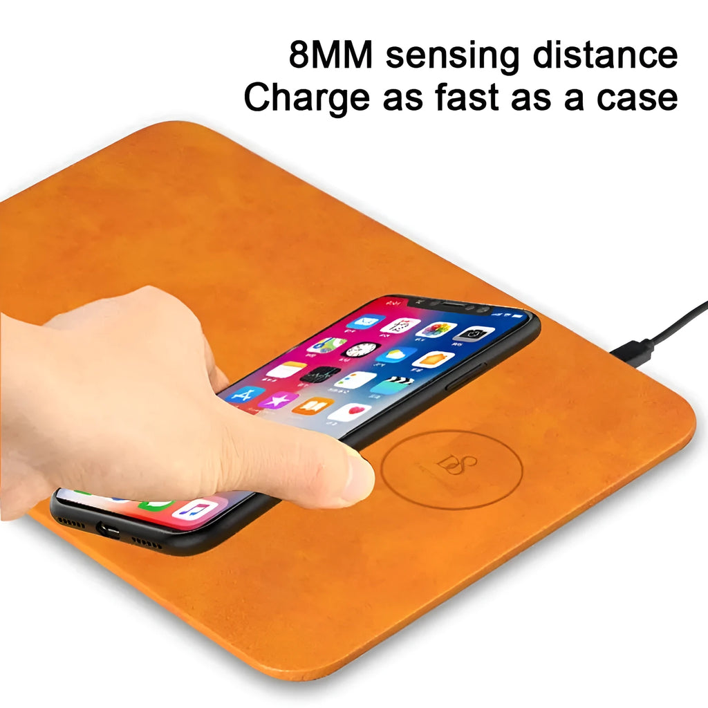 Brown leather wireless charging mouse pad on a wooden desk with a smartphone charging on its surface.