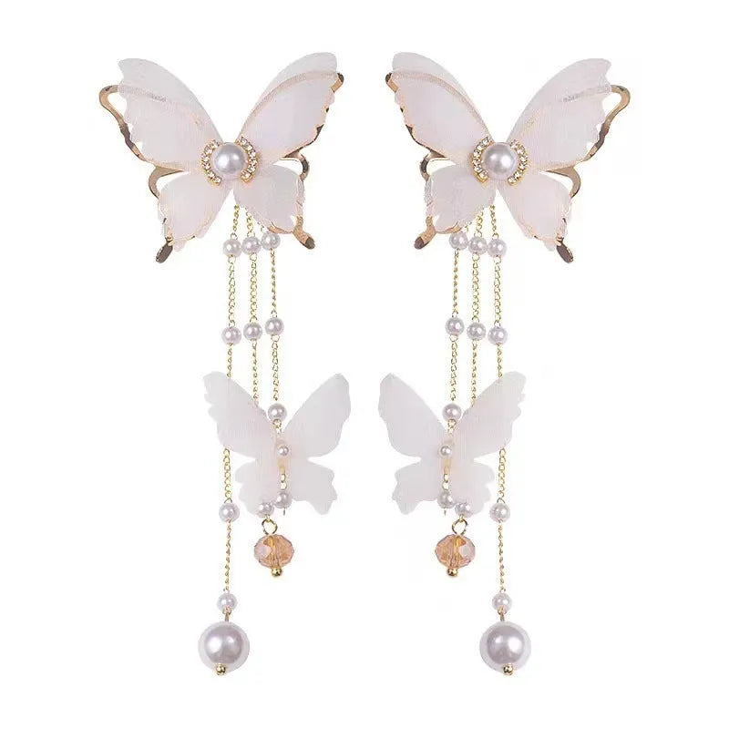 White butterfly-shaped dangling earrings with rhinestones, a pearl, and a fine chain on a plain background.