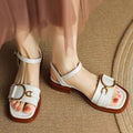 Women's black thick-soled leather sandals with a round toe and button fastening on a white background.