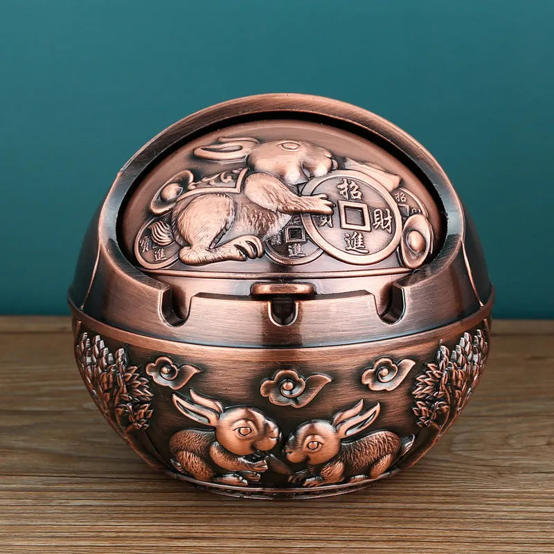 Bronze and red copper alloy decorative ashtray with smoke-extinguishing slot on a table.