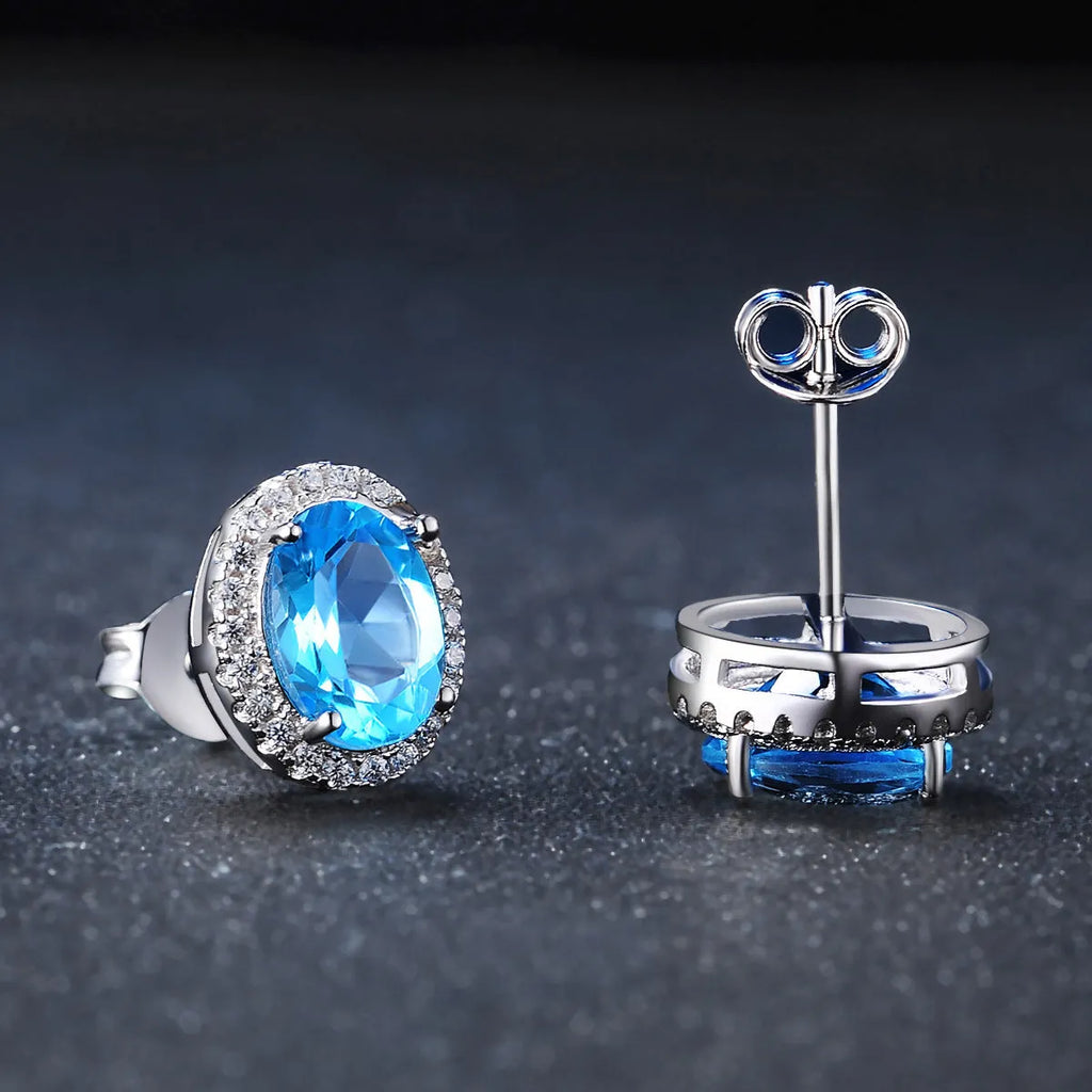 Four-piece sterling silver jewellery set with blue topaz gems: earrings, ring, pendant, and necklace on a geometry pattern.