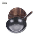 Handmade black iron wok pan with a long wooden handle on a kitchen counter.