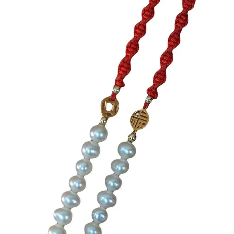 Close-up of a women's pearl and braided red rope bracelet with a gold-plated geometric fu character charm.