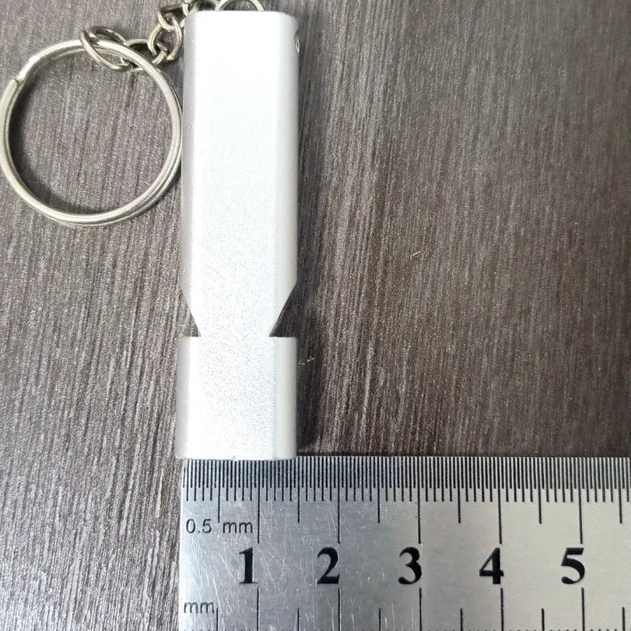 Close-up of a silver aluminium alloy double-hole outdoor survival whistle on a dark background.