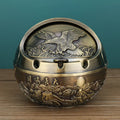 Bronze and red copper alloy decorative ashtray with smoke-extinguishing slot on a table.
