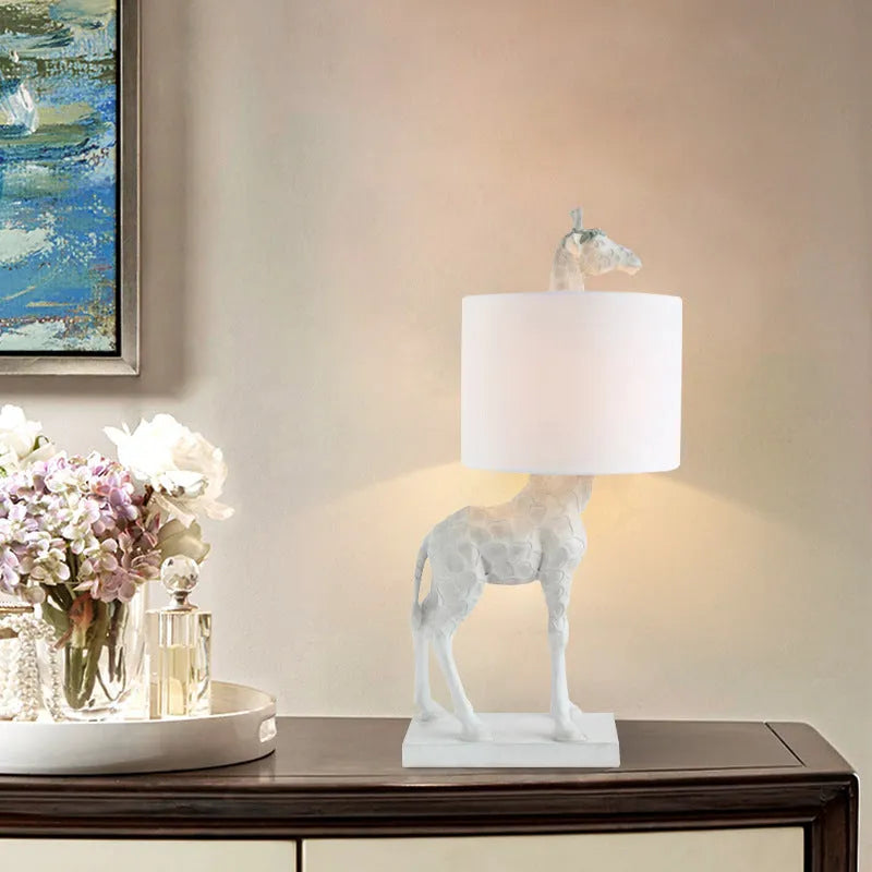 White giraffe table lamp with cloth shade on wooden bedside table