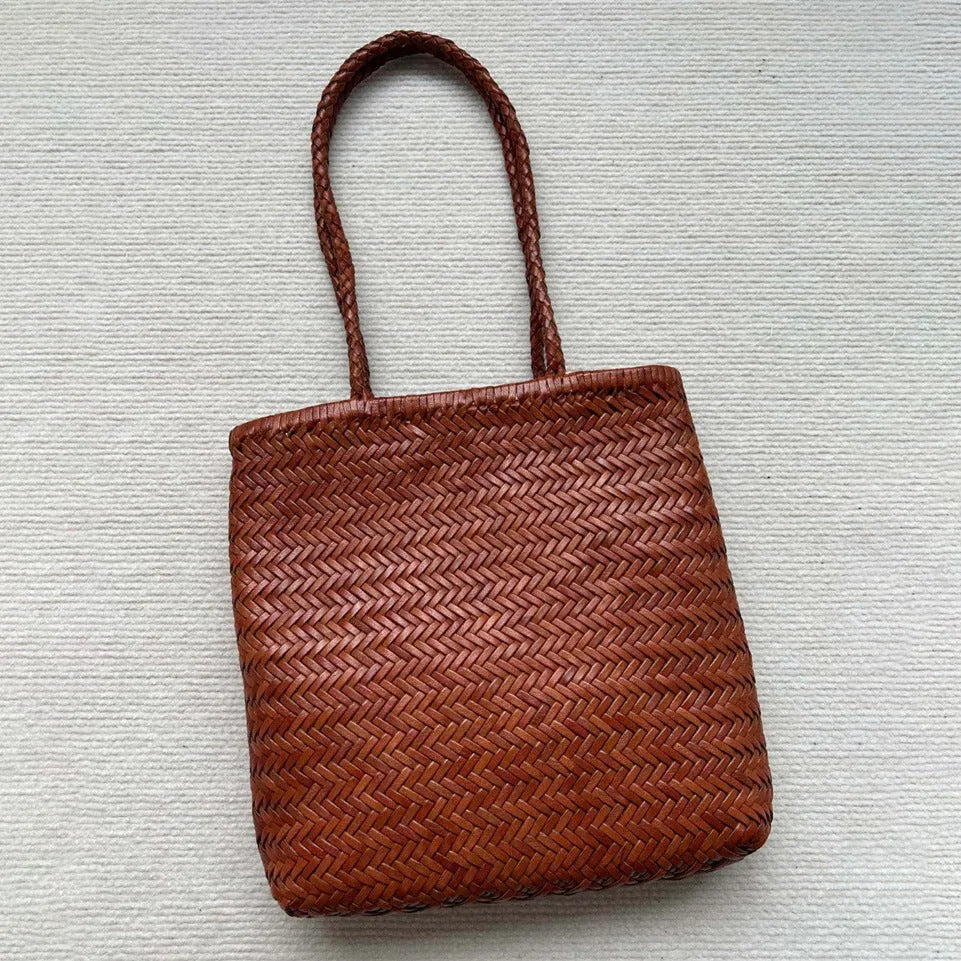 Brown handmade woven leather tote bag with a three-dimensional front pocket and shoulder strap.
