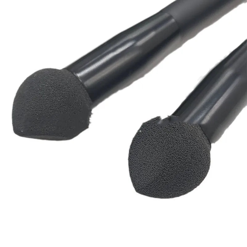 Black wooden handle concealer brush with a grey sponge tip applicator angled for under eye use.