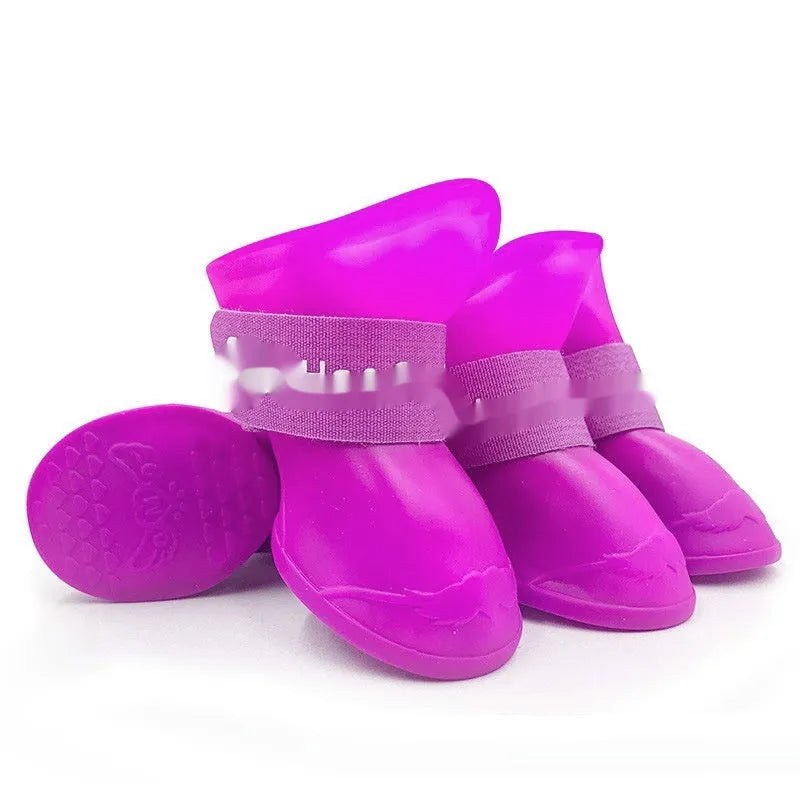 Set of four colourful rubber dog rain shoes with anti-slip soles on a wet surface.