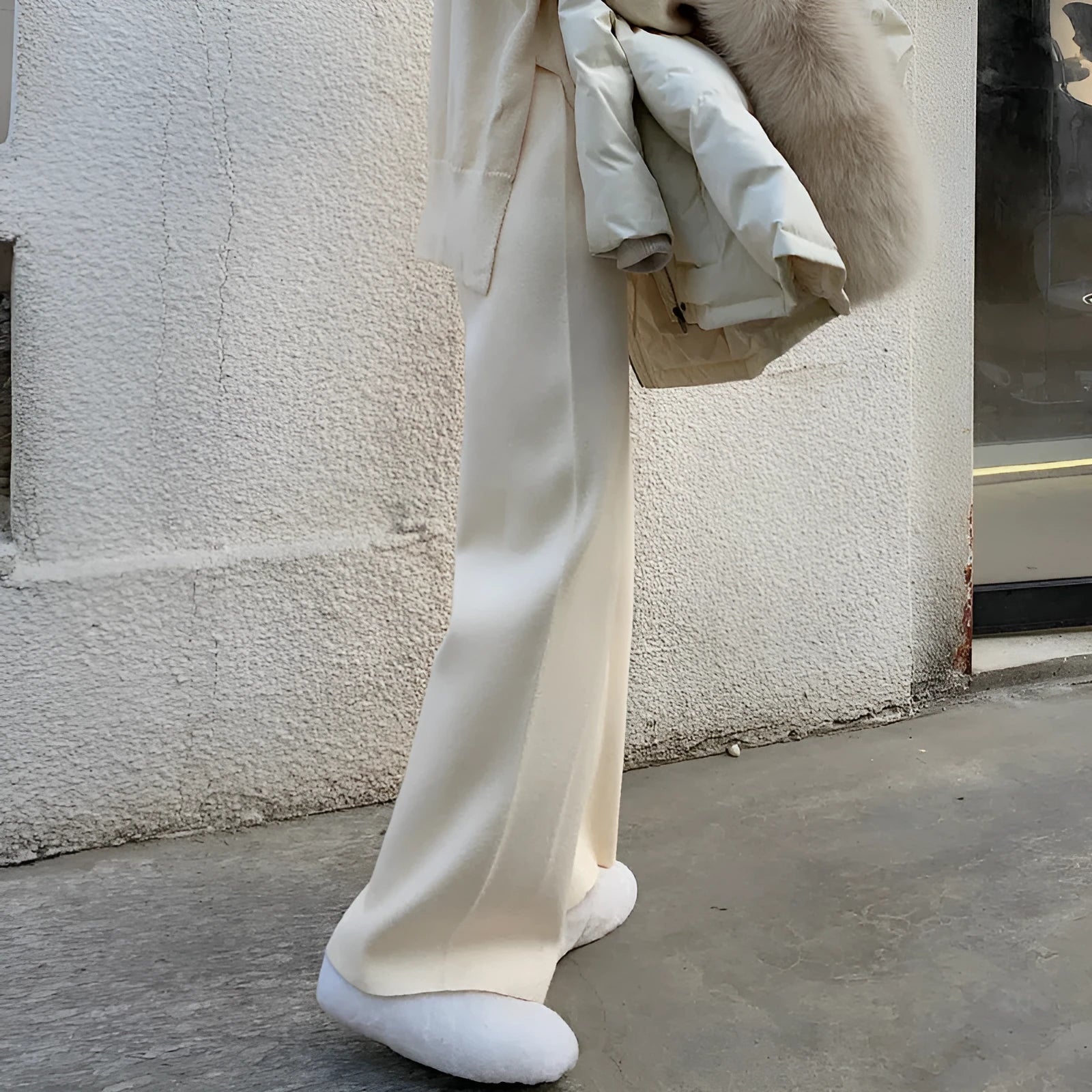 Woman wearing cream white knitted high-waist wide-leg winter trousers.