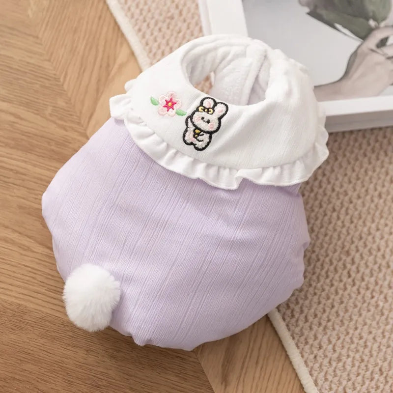 Small dog wearing a lavender bunny embroidered pet coat with white ruffled collar and fluffy pom-pom tail