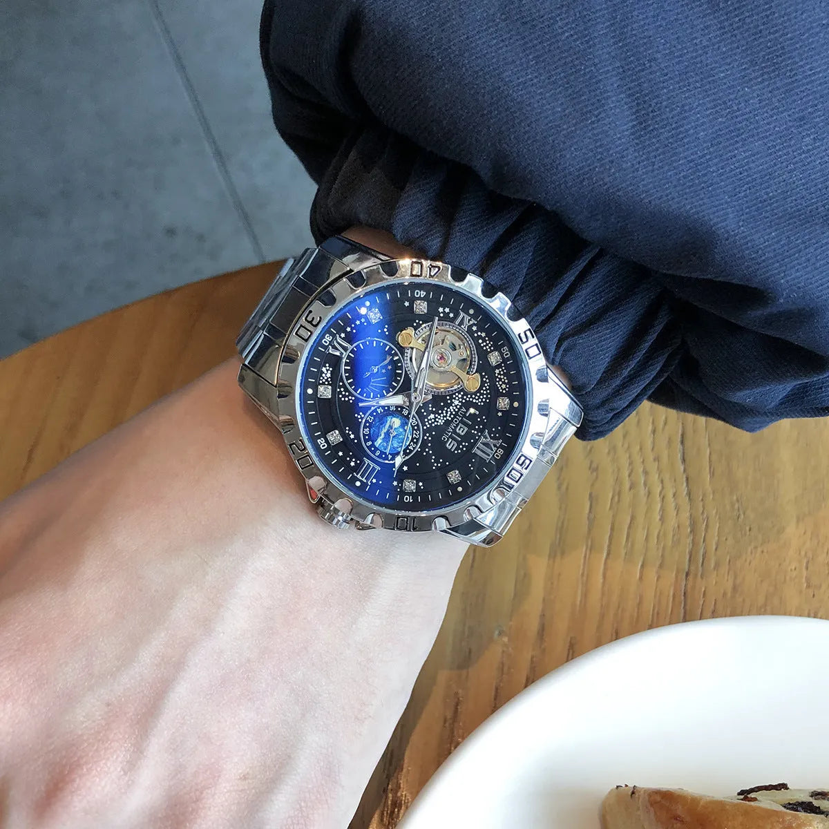 Men's silver automatic watch with black starry dial and leather strap on wrist.